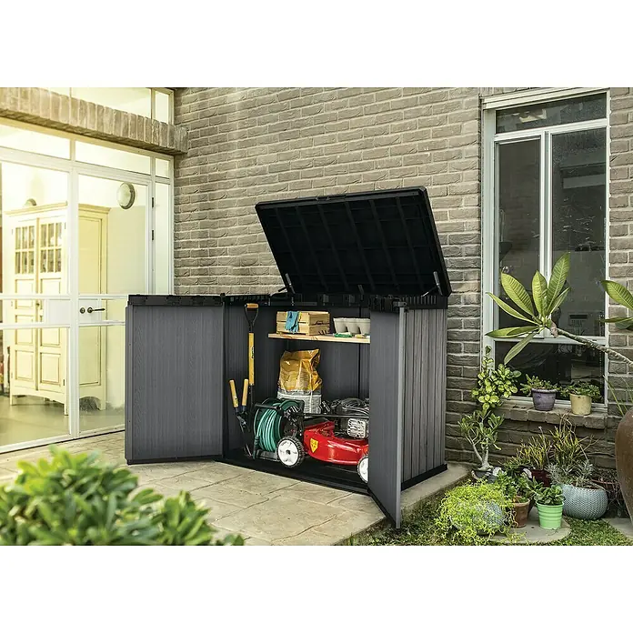 Keter Truhe Store it out Darwin - L x B x H: 80 x 140 x 118 cm, Stormgrey, Kunststoff - Das Bild zeigt eine geöffnete, graue Gartenbox, die mit Gartengeräten wie einem Rasenmäher und einer Harke gefüllt ist.