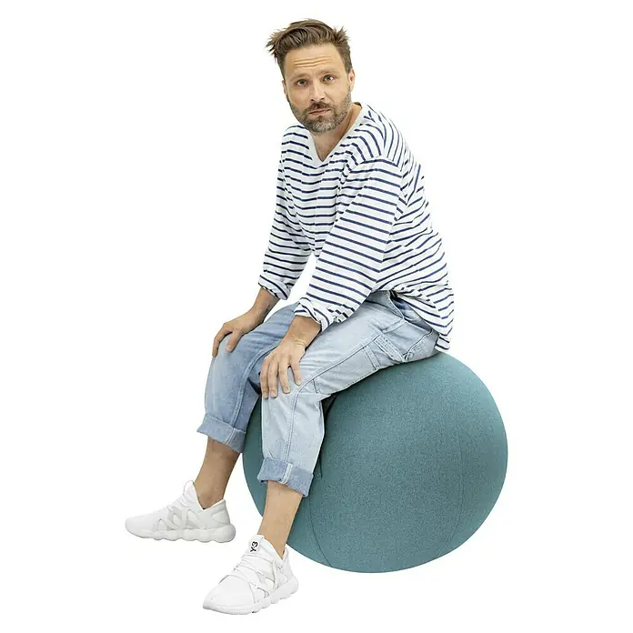 Sitting Ball Gymnastikball Felt - Aquarius, Durchmesser: 65 cm, 100 % Polyester - Mann sitzt auf einem blauen Gymnastikball, trägt ein gestreiftes Hemd und weiße Turnschuhe. Bequemer und stilvoller Bürostuhl für aktive Arbeit.