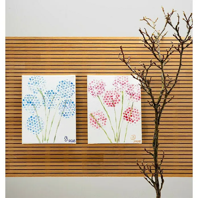 Glorex Keilrahmen Art 4 You - 30 x 24 cm, 3-fach grundiert, 330 g/m² - Nahaufnahme von zwei Leinwandbildern mit blauen und rosafarbenen Pusteblumen auf einer hölzernen Wand, neben einem Ast.