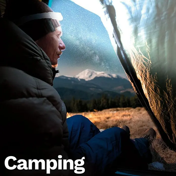 Stirnlampe Handy Brite Work Light - 260 lm - Mann im Zelt mit Stirnlampe, der die Sterne und die Berglandschaft bewundert. Campingausrüstung für Abenteuer in der Natur.