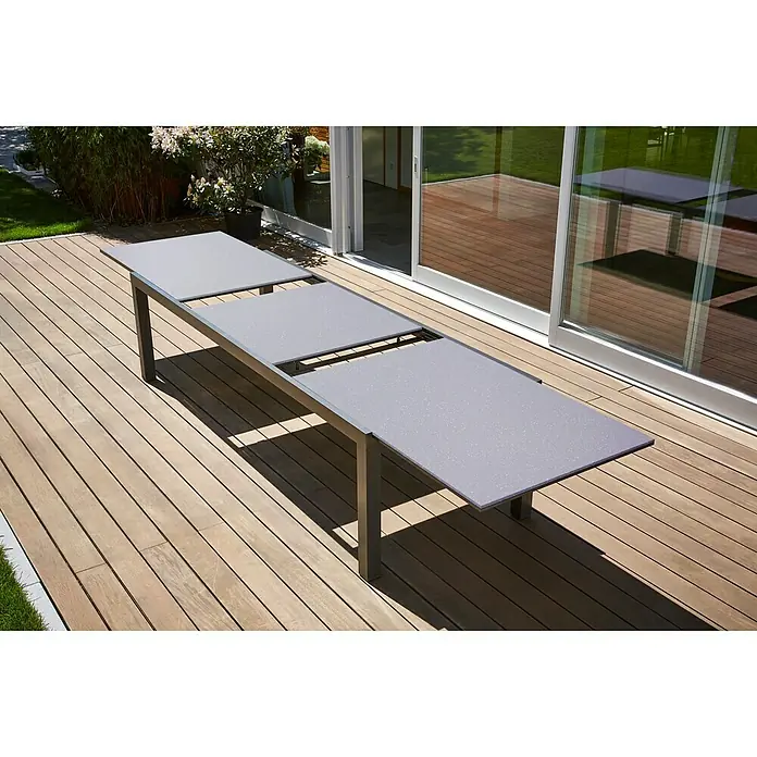 Sunfun Maja Gartentisch - L x B x H: 280 x 100 x 75 cm, Aluminium, Glas, Rechteckig, Night-Grey, Ausziehbar - Ausziehbarer Gartentisch auf einer Holzterrasse, ideal für Mahlzeiten im Freien. Der Tisch hat eine graue Oberfläche und ein modernes Design.