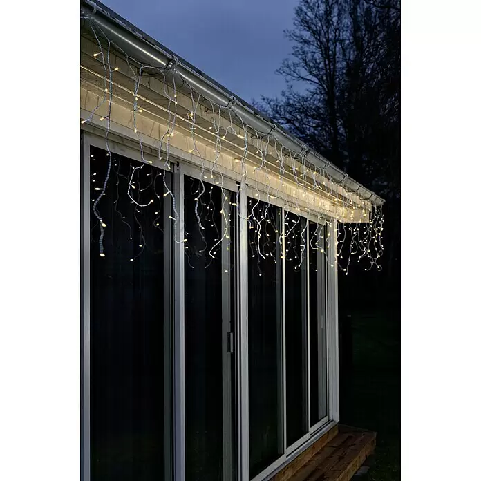 Konstsmide LED-Lichtervorhang Eisregen - Außen, 0,75 m, Bernstein, 200 Stk., Netzbetrieben - Warmweiße LED-Eiszapfenlichter mit weißem Kabel schmücken die Außenfassade eines Gebäudes, leuchtend vor dem Dämmerungshimmel.