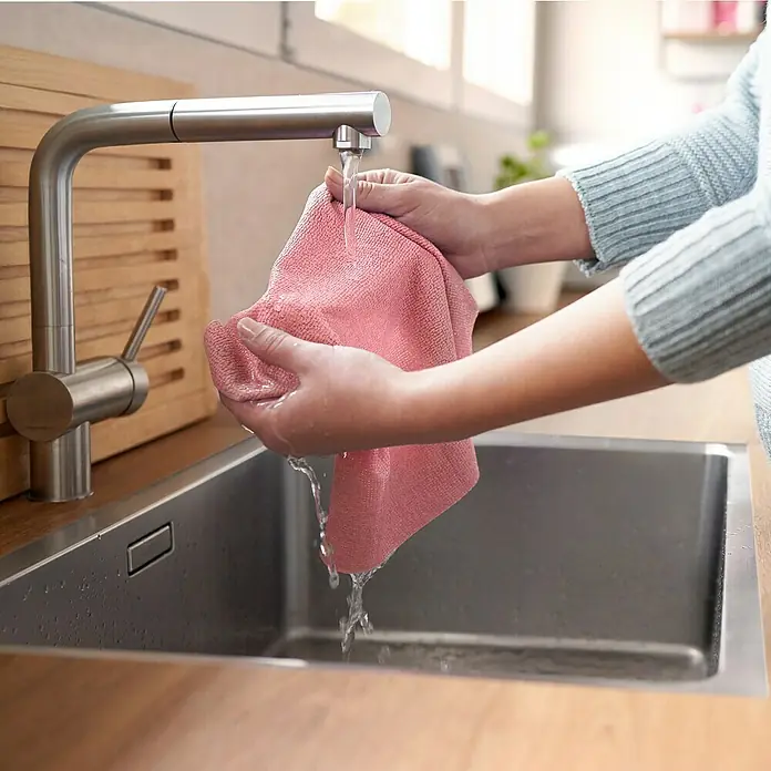 Vileda Universalreinigungstücher Actifibre Soft Touch - 2 Stk., Mikrofaser - Eine Person wäscht ein rosa Tuch unter einem Wasserhahn in einer Edelstahlspüle. Der Wasserhahn ist modern und aus gebürstetem Metall.