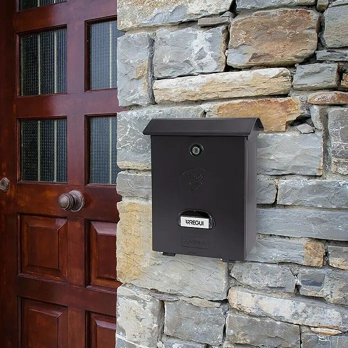 Arregui Classic Buzón de pared E-107 - L x An x Al: 27 x 11 x 34,6 cm, Negro, Plástico - Un buzón negro Arregui montado en una pared de piedra junto a una puerta de madera. Ideal para recibir correo.