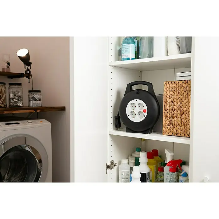 Brennenstuhl Kabeltrommel Vario Line VL2-X - Kunststoff, 10 m, H05VV-F, IP20 - Eine Mehrfachsteckdose mit Kabelaufroller in einem weißen Schrank, umgeben von Reinigungsutensilien und einem Weidenkorb. Praktische Stromversorgung.