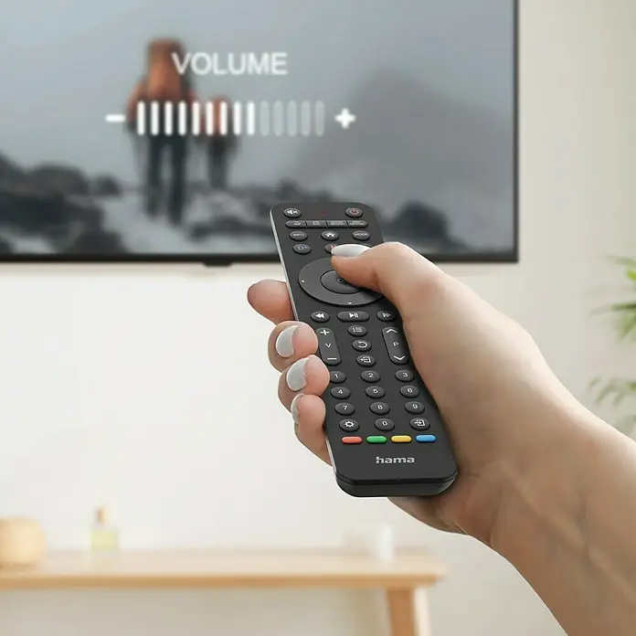 Hama Universal-Fernbedienung 4 in 1 - 202 x 41 x 21 mm, Passend für: TV, Set-Top-Box, Sat-Receiver, Soundbar, DVB-T-Receiver, Kabel-Receiver, Blu-ray-Player, Verstärker - Eine Hand hält eine Hama-Fernbedienung vor einem verschwommenen Fernsehbildschirm, auf dem eine Lautstärkeregelung angezeigt wird.