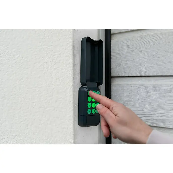 Schellenberg Funk-Codetaster Powerlift - Anzahl Kanäle: 4 Stk., Passend für: Schellenberg Garagentor- und Drehtorantriebe - Eine Hand, die eine wetterfeste Tastatur mit grün beleuchteten Ziffern bedient, die an einer weißen Wand montiert ist.