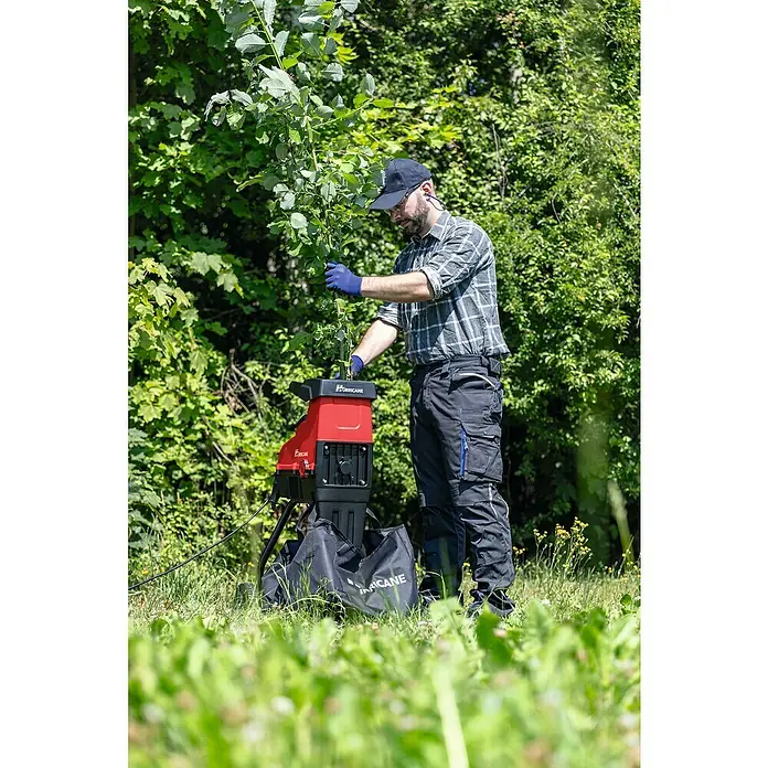 Hurricane Elektro-Leisehäcksler HLH-S-2800 - Max. Aststärke: 44 mm, 2.800 W - Mann benutzt einen HURRICANE Häcksler im Garten. Er trägt Handschuhe, um Äste in den robusten, roten Gartenhäcksler einzuführen.