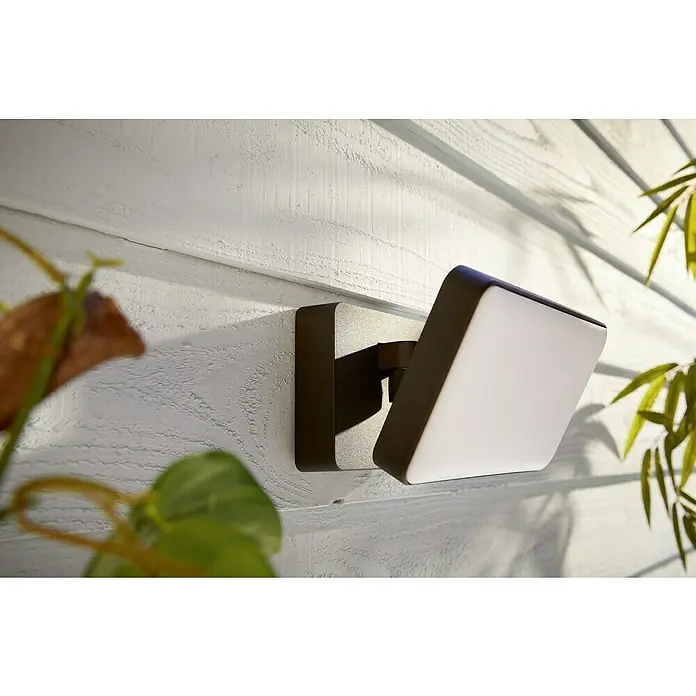 Philips Hue LED-Strahler White & Color Ambiance - 15 W, L x B x H: 22 x 16 x 15,3 cm, Schwarz, RGBW - Nahaufnahme einer modernen Außenleuchte mit rechteckigem Design in Braun und Weiß an einer weißen Holzwand.