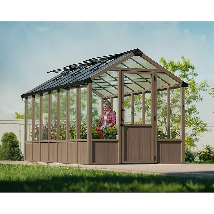 Palram – Canopia Invernadero Natura - Medidas ext. (An x Pr): 249 x 500 cm, Plástico, 4 mm, Natural - Un invernadero con una mujer cuidando plantas, que ofrece un ambiente ideal para cultivar flores y verduras.