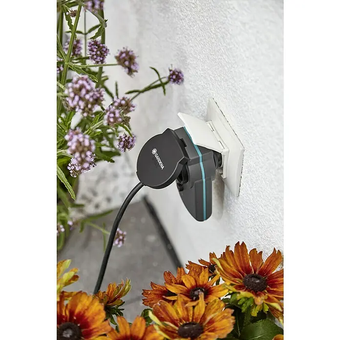 Gardena Smart system Stecker Smart Power - Passend für: Gardena Smart System - Gardena Smart Power Adapter in einer Steckdose, umgeben von bunten Blumen. Ermöglicht die smarte Steuerung von Gartengeräten.