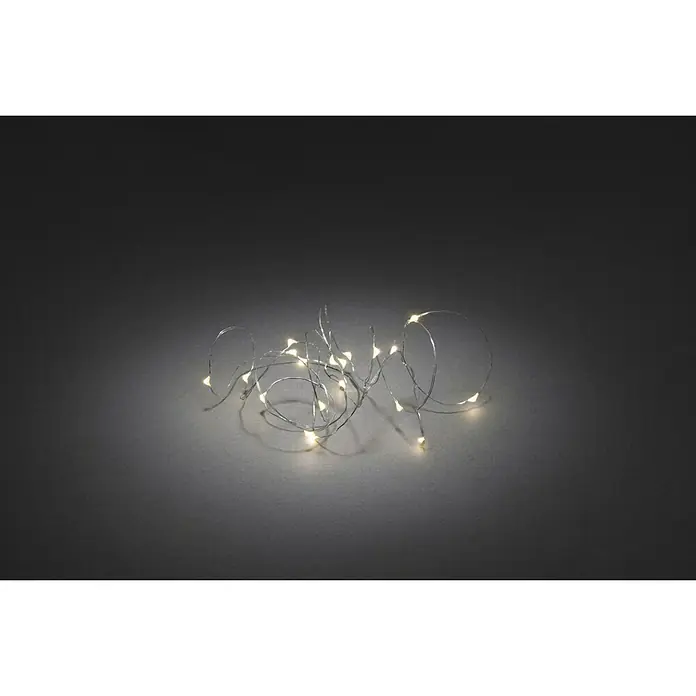 Konstsmide LED-Lichterkette - Innen, Lichtfarbe: Warmweiß, Anzahl Leuchtmittel: 20 Stk., Batteriebetrieben, Silber - Das Bild zeigt eine Lichterkette mit vielen kleinen, warm leuchtenden LED-Lampen auf einem silbernen Draht. Die Lichterkette liegt auf einem dunklen Untergrund.