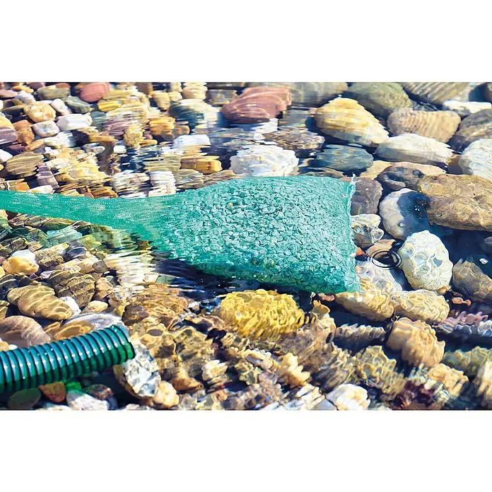 Oase AquaActiv Zeolith Pondlith Filtermaterial - 2,5 kg - Bachbett mit einem grünen Netzbeutel voller Steine im Wasser und einem grünen Schlauch am Ufer.