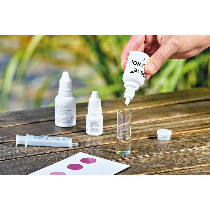 Oase AquaActiv Wasseranalyse-Set - Geeignet für: Gartenteiche - Ein Oase Wassertest-Set wird auf einem Holztisch mit einem transparenten Behälter und Reagenzflaschen für die Wasseranalyse verwendet.