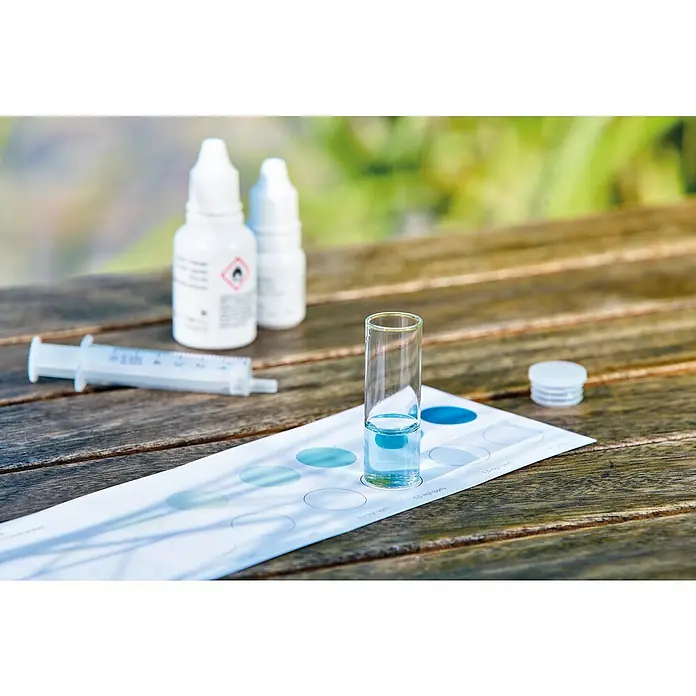 Oase AquaActiv Wasseranalyse-Set - Geeignet für: Gartenteiche - Ein Wasserqualitäts-Testkit mit Fläschchen, Spritze, Farbtabelle und einem Glasröhrchen mit Wasserprobe auf einem Holztisch im Freien.