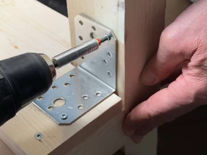 Mit einem Winkelverbinder wird das Rahmenholz mit dem Holzbrett verbunden