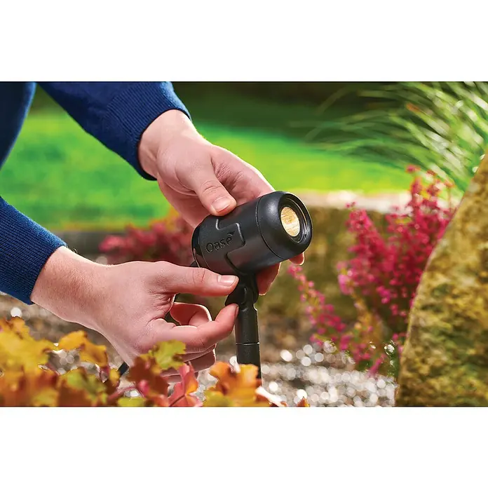 Oase LED-Spotstrahler LunAqua Connect S Set 3​ - Anzahl LED: 3 Stk., Warmweiß - Eine Person justiert einen schwarzen Oase Gartenstrahler vor einem Blumenbeet, um die Gartenbeleuchtung zu optimieren.