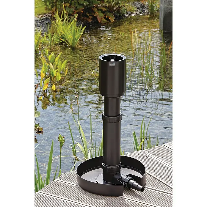 Oase Saugfilter AquaSkim 20 - Ausstattung: Saug- und Regulierungsstutzen - Nahaufnahme einer schwarzen Oase-Gartenpumpe, die auf einem Holzsteg neben einem Teich steht.