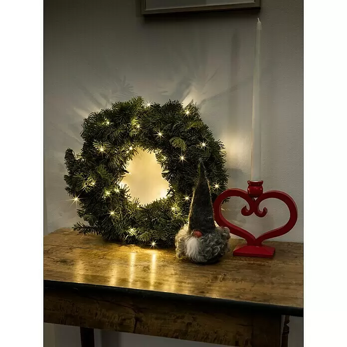 Konstsmide LED-Lichterkette Microsnoer LED - Innen, Lichtfarbe: Warmweiß, Anzahl Leuchtmittel: 35 Stk., Netzbetrieben - Eine festliche Anordnung auf einem Holztisch mit beleuchtetem Tannenkranz, grauem Wichtel und rotem Herz-Kerzenhalter mit weißer Kerze.