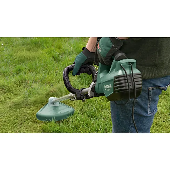 Bosch Elektro-Freischneider AFS 23-37 - 1.000 W, Schnittbreite Faden: 37 cm, Schnittbreite Messer: 23 cm - Nahaufnahme eines Benutzers, der einen grünen Bosch Rasentrimmer zum Trimmen von Gras verwendet.