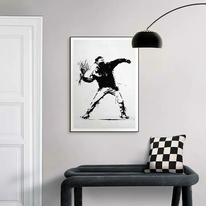 Reinders Bild Slim Frame Black - Flower Thrower, B x H: 50 x 70 cm - Das Bild zeigt ein Banksy-Kunstwerk mit einem Blumenwerfer, gerahmt und an einer grauen Wand über einer Bank mit Schachbrettmuster-Kissen aufgehängt.