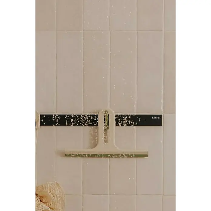 Cosmic Guía de pared Alife - Negro, L x An x Al: 0,4 x 40 x 2,7 cm - Un limpiacristales de ducha beige cuelga de un soporte negro con puntos blancos en una pared de baño alicatada en blanco.