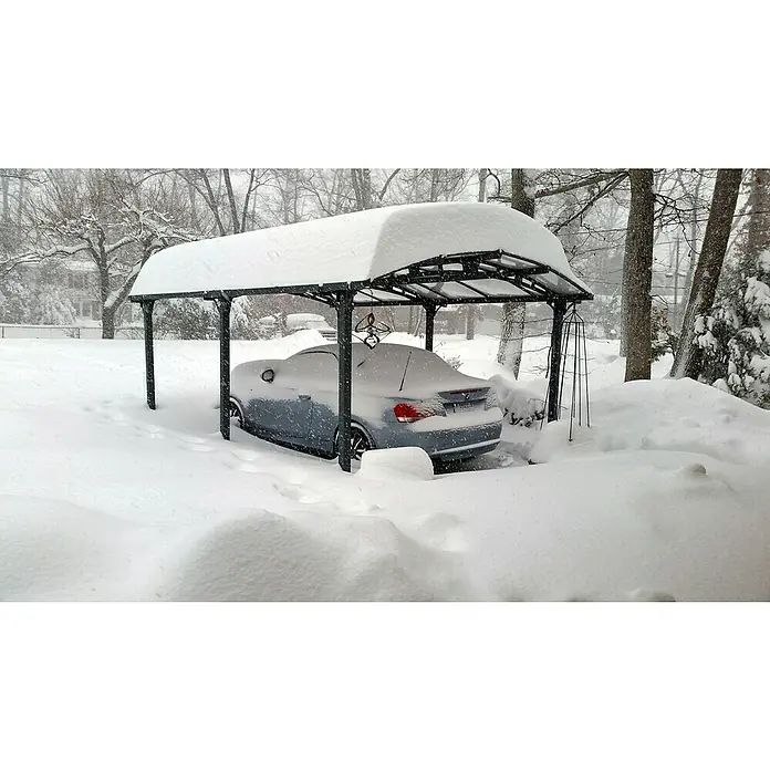 Palram – Canopia Carport Arcadia - Medidas ext. (An x Pr): 3,59 x 3,59 m, Carport doble, Gris - Un BMW convertible plateado se encuentra bajo una cochera cubierta de nieve, rodeado de una gruesa capa de nieve, destacando la resistencia invernal del coche.