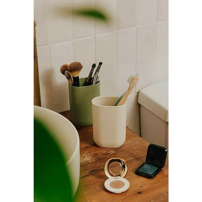 Cosmic Portacepillos Alife - Negro - Una naturaleza muerta de baño con dos tazas, brochas de maquillaje, un cepillo de dientes y dos polveras cosméticas sobre una mesa de madera.