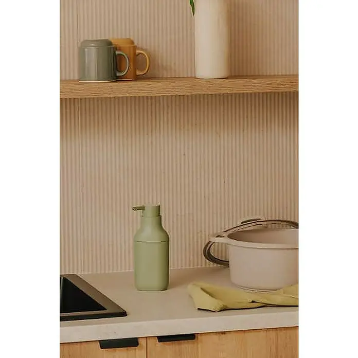 Cosmic Dosificador de jabón Alife - Verde - Primer plano de un frasco de jabón, una olla y un paño amarillo sobre una encimera de cocina.