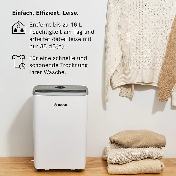 Bosch Luftentfeuchter Dry 4000 - Entfeuchtungsleistung: 16 l/Tag, Weiß - Abgebildet ist ein Bosch Luftentfeuchter vor einem Stapel gefalteter Pullover und zwei hängenden Strickjacken.
