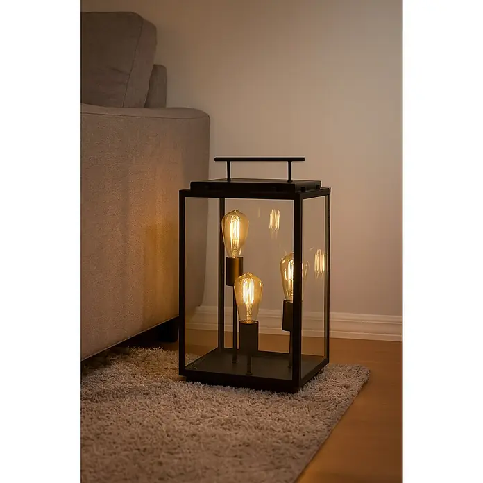 Starlux Lámpara decorativa Latiano - L x An x Al: 28 x 28 x 50 cm, E27 - Esta imagen muestra una elegante lámpara de linterna negra con bombillas sobre una alfombra, creando un ambiente cálido y acogedor.
