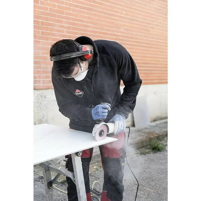 Rubi Disco de corte Slither Superpro - Ø x Es: 125 x 2,2 mm - Hombre cortando baldosas con una amoladora RUBI. Lleva equipo de protección para protegerse de lesiones mientras trabaja.