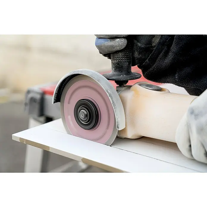 Rubi Disco de corte Slither Superpro - Ø x Es: 125 x 2,2 mm - Primer plano de una persona que utiliza una amoladora en una baldosa blanca. Los guantes protectores protegen las manos durante el proceso.