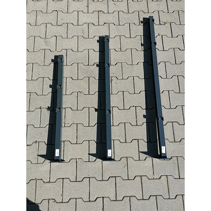 Peddy Shield Zaunpfosten - Höhe: 110 cm, Anthrazit, Zum Aufschrauben - Drei dunkelgraue Zaunpfosten aus Metall, die in der Größe variieren, liegen auf einem Pflastersteinboden und werfen Schatten.