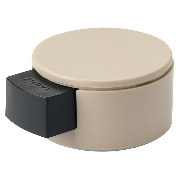 Inofix Tope de puerta 2420 - Plástico, Beige - Primer plano de un tope de puerta cilíndrico beige con una cuña rectangular negra. Un tope de puerta práctico para el uso diario.