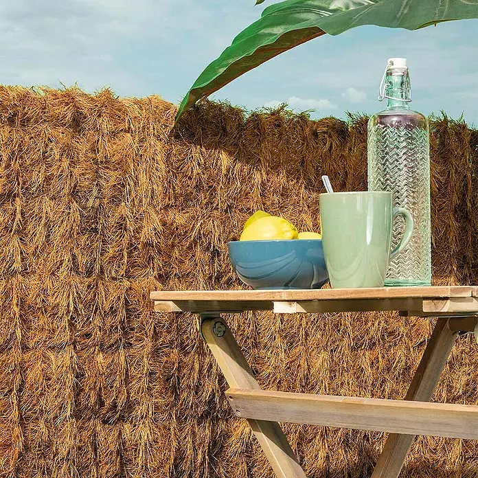 Nortene Sichtschutzmatte Coconatur - 300 x 100 cm - Eine Wasserflasche und eine Tasse stehen neben einer Schale Zitronen auf einem Holztisch vor einem natürlichen Hintergrund.