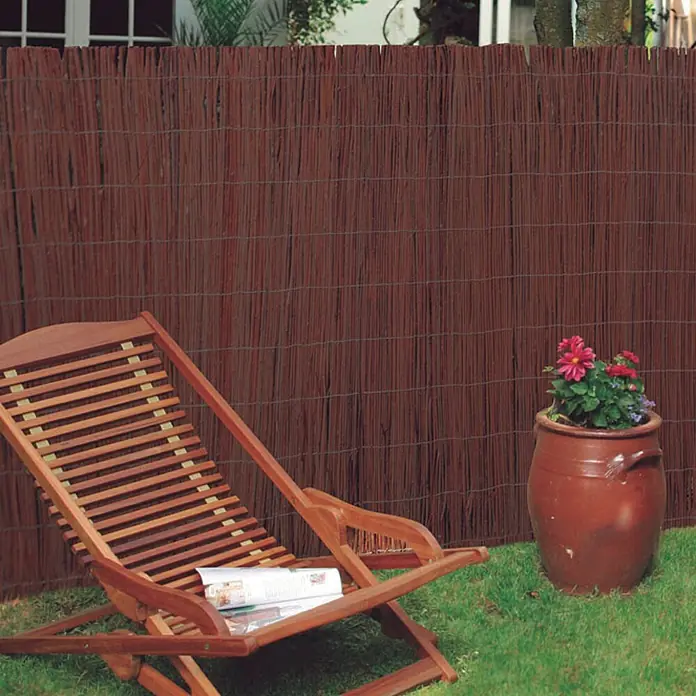 Nortene Weidenmatte - 300 x 100 cm, Weide, Braun - Blick auf einen Sichtschutzzaun aus Rohrgeflecht im Garten, neben einem Liegestuhl und einem Blumentopf. Ideal für Privatsphäre und Dekoration.