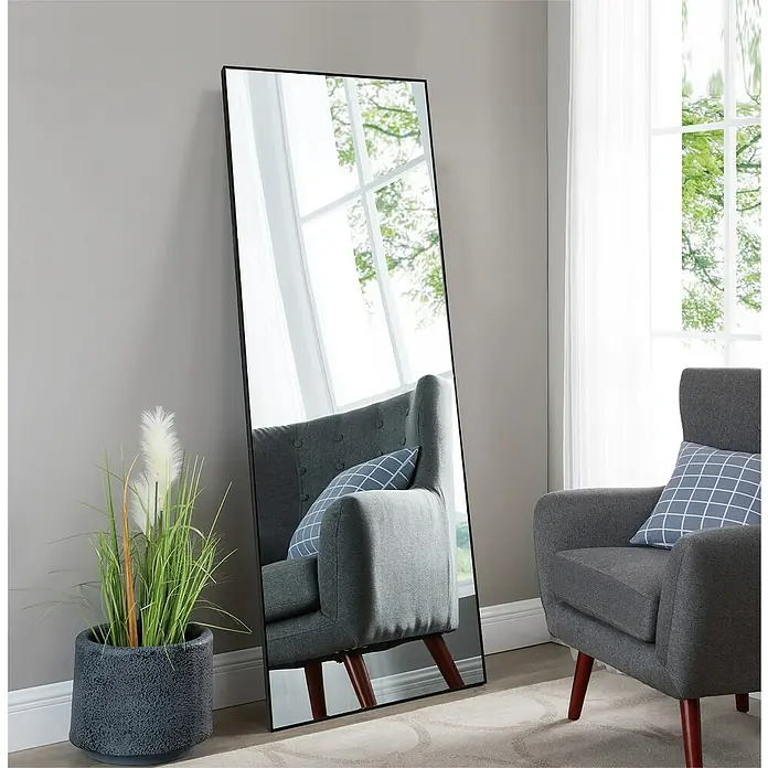 Rahmenspiegel Levi - 60 x 180 cm, Schwarz, Aluminium - Schwarzer Ganzkörperspiegel lehnt an einer Wand, daneben ein Sessel und ein Topf mit Pflanzen.