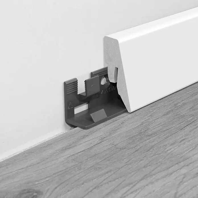 LOGOCLIC Sockelleiste K40 C Weiß - 260 cm x 12 mm x 40 mm, MDF - Eine weiße Fußleiste mit einem grauen Befestigungsclip, die an einer Wand und einem Boden befestigt ist.