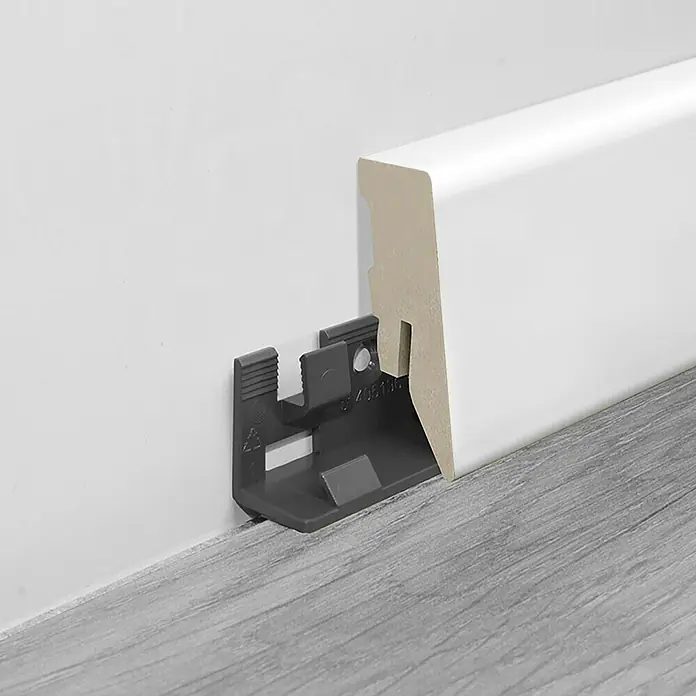 LOGOCLIC Sockelleiste Weiß - 260 cm x 18 mm x 50 mm, MDF - Nahaufnahme einer Sockelleiste mit Befestigungsclip an einer Wand über einem grauen Boden.