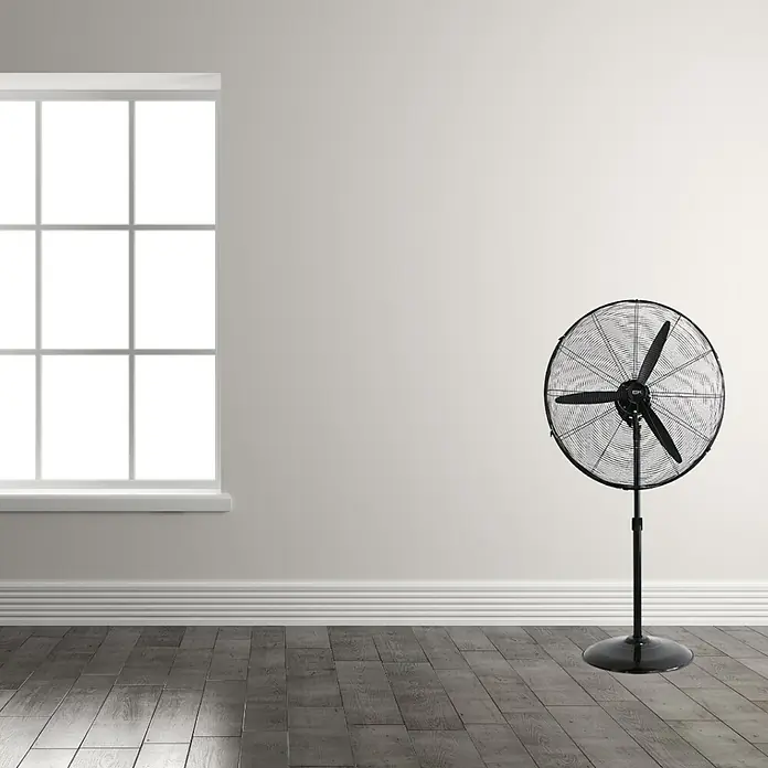 EDM Ventilador de pie industrial - Negro, 66 cm, 117 cm - 156 cm - Un ventilador de pie negro en una habitación con ventana y suelo de madera que ofrece una brisa refrescante.