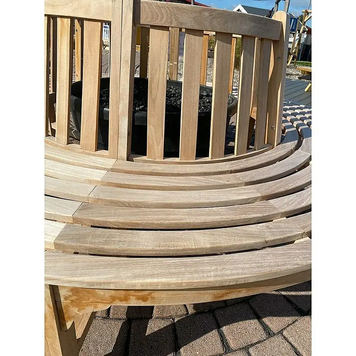 Joda Baumbank 360° - Ø x H: 220 x 90 cm, Teak, Naturbraun - Nahaufnahme einer runden Holzbank um einen Feuerkorb. Die Bank besteht aus hellen, gebogenen Holzlatten und bietet Sitzplätze im Freien.