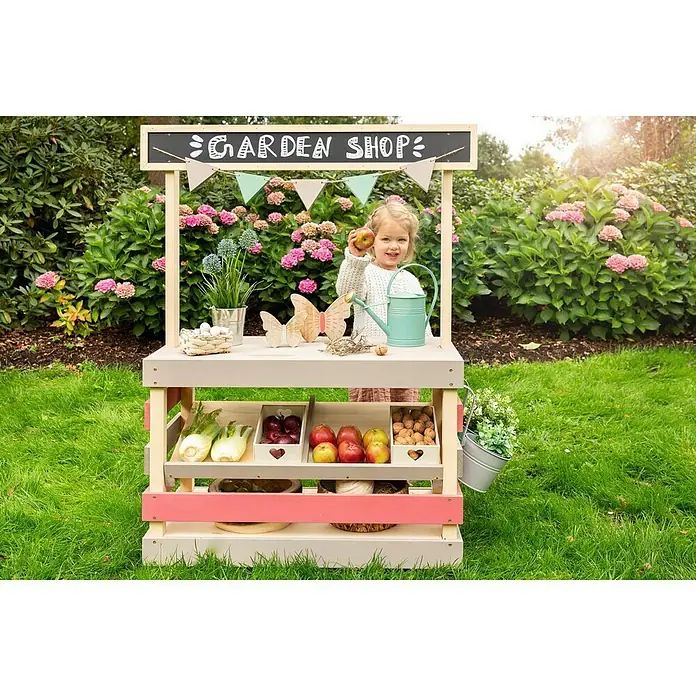 Muddy Buddy Kinder-Kaufladen Garden Friend - 90 x 40 x 115 cm, Holz, Natur/Warmgrau/Malvenrosa - Eine junge Gärtnerin präsentiert ihren farbenfrohen Kaufladen mit frischem Obst, Gemüse und dekorativen Pflanzen. Ein idyllisches Gartenspielparadies für Kinder.