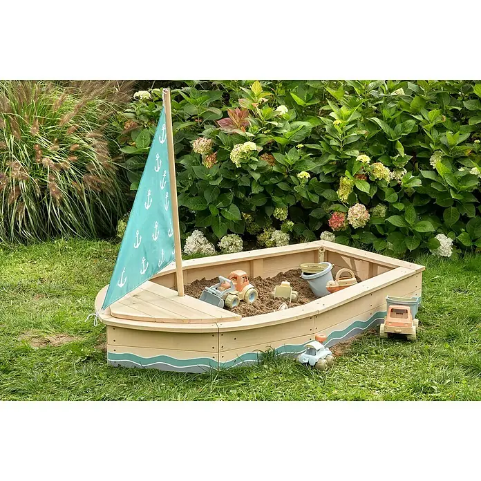 Muddy Buddy Sandkasten Anchor Lover - L x B x H: 160 x 90 x 102 cm, Holz - Dieses Bild zeigt einen Sandkasten in Form eines Bootes mit Spielzeug, das im Gras steht, ideal für Kinder zum Spielen im Freien.