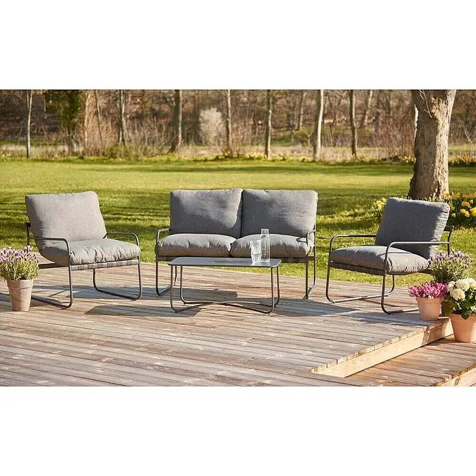 Conjunto de muebles Theodor - 4 pzs., Acero/Poliéster, Antracita - Conjunto de muebles de exterior con mesa, sofá de dos plazas y dos sillas de tela gris y metal oscuro sobre una terraza de madera con plantas.