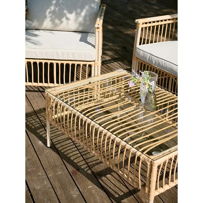 Conjunto de muebles Neel - 4 pzs., Acero/Ratán sintético, Natural/Beige - Primer plano de una mesa de centro de ratán con tapa de cristal, complementada con sillas de ratán a juego con cojines claros para un ambiente relajado al aire libre.