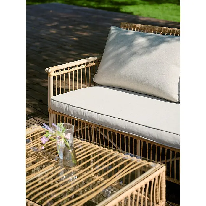 Conjunto de muebles Neel - 4 pzs., Acero/Ratán sintético, Natural/Beige - Primer plano de un sofá de ratán con cojines y una mesa con flores en un patio.