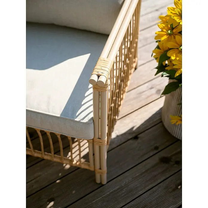 Conjunto de muebles Neel - 4 pzs., Acero/Ratán sintético, Natural/Beige - Primer plano de una silla de mimbre con cojines claros y un jarrón con flores amarillas en un patio de madera.
