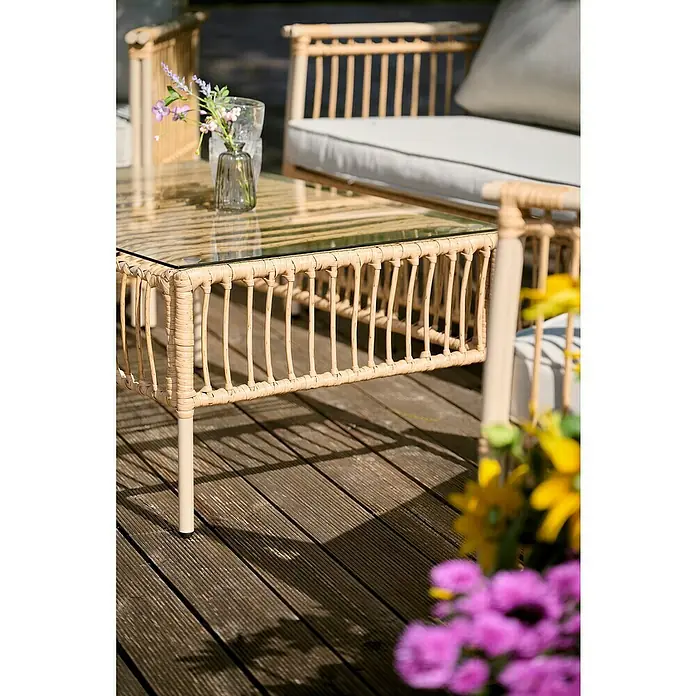 Conjunto de muebles Neel - 4 pzs., Acero/Ratán sintético, Natural/Beige - Primer plano de una mesa de centro de ratán con tapa de cristal sobre una terraza de madera, una invitación a relajarse al aire libre.