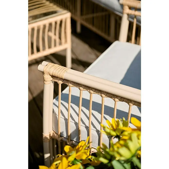 Conjunto de muebles Neel - 4 pzs., Acero/Ratán sintético, Natural/Beige - Elegante mobiliario de ratán con cómodos cojines y flores amarillas en primer plano, creando un ambiente relajado para espacios exteriores.